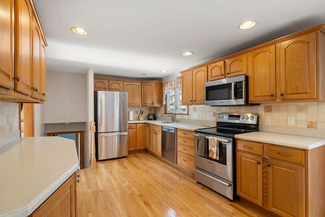 kitchen featuring stainless steel appliances, light countertops, backsplash, a sink, and light wood-type flooring