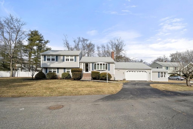 split level home with a garage, a chimney, fence, and a front yard