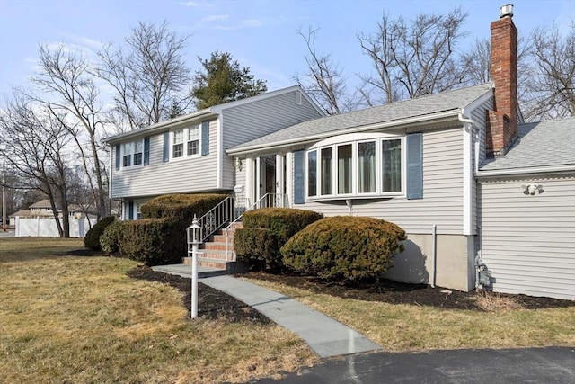 split level home with a shingled roof, a chimney, and a front yard