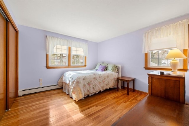 bedroom featuring light wood-type flooring, multiple windows, a baseboard radiator, and a closet