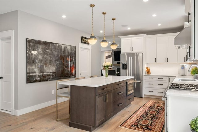 35 E St, Middleton, MA 01949 - kitchen with stainless steel appliances, wall chimney exhaust hood, dark brown cabinets, light wood-type flooring, and white cabinetry