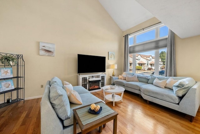 living area with baseboards, high vaulted ceiling, wood finished floors, and a glass covered fireplace