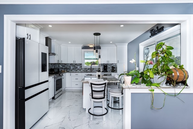 kitchen featuring backsplash, stainless steel range oven, refrigerator, wall chimney exhaust hood, and pendant lighting