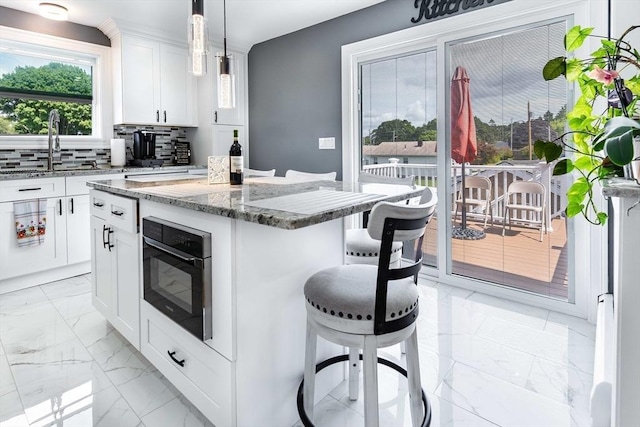 kitchen featuring a breakfast bar, marble finish floor, tasteful backsplash, a sink, and oven