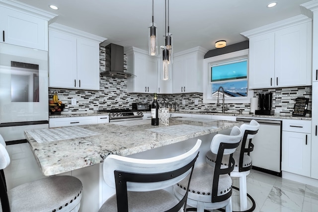 kitchen featuring wall chimney exhaust hood, white cabinetry, a breakfast bar area, and hanging light fixtures