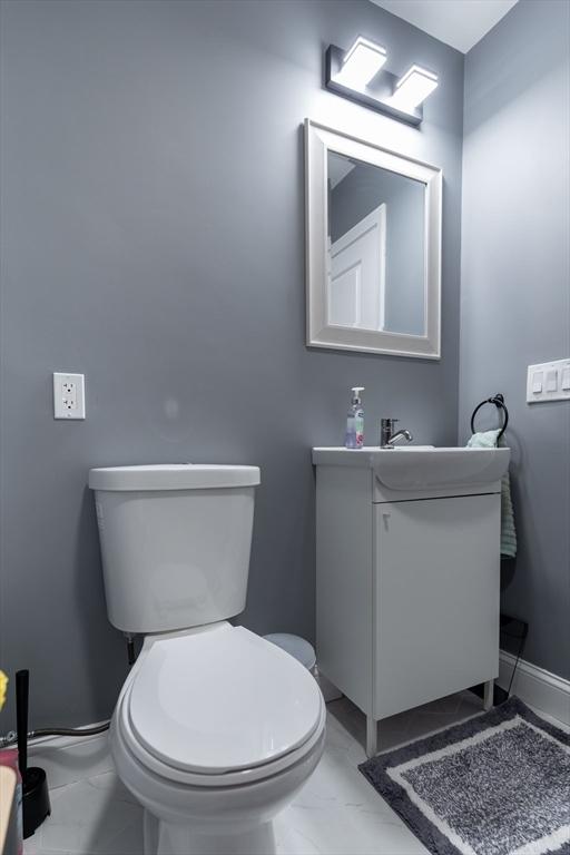 half bathroom featuring marble finish floor, baseboards, vanity, and toilet