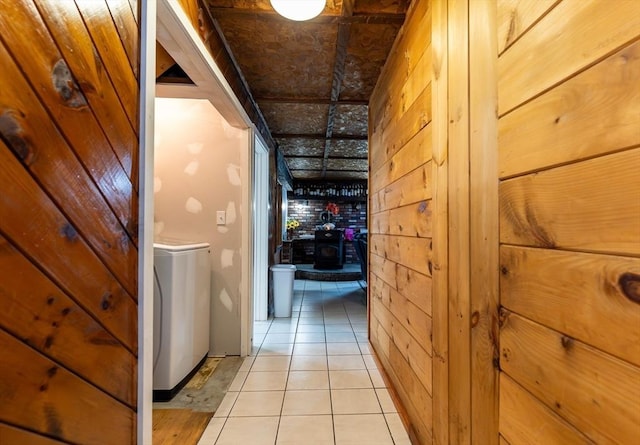 hall with light tile patterned floors, wood walls, and washer / dryer