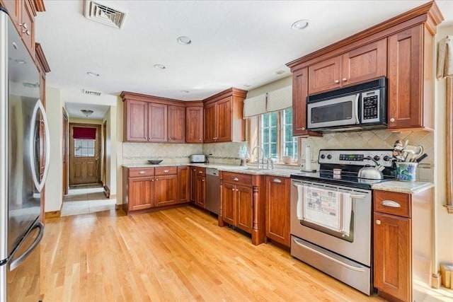 11 Tara Dr, Pembroke, MA 02359 - kitchen with appliances with stainless steel finishes, light wood-style flooring, decorative backsplash, light stone countertops, and brown cabinetry