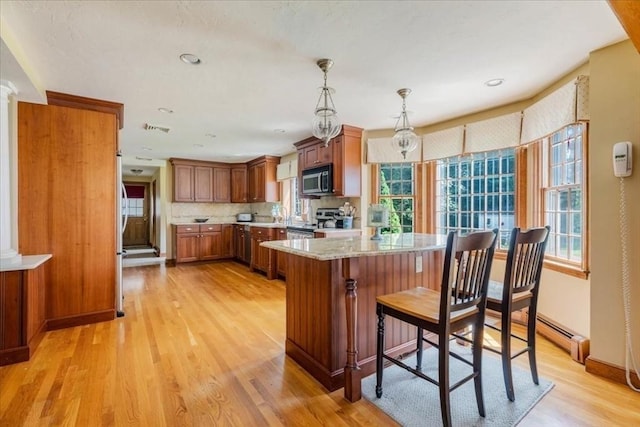 11 Tara Dr, Pembroke, MA 02359 - kitchen featuring appliances with stainless steel finishes, light wood-type flooring, brown cabinetry, pendant lighting, and backsplash