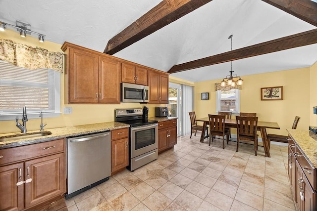 kitchen featuring appliances with stainless steel finishes, light stone counters, a sink, and decorative light fixtures