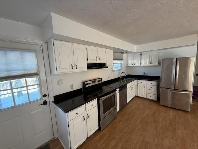 kitchen featuring appliances with stainless steel finishes, sink, a textured ceiling, dark wood-type flooring, and white cabinets