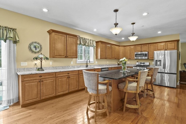 kitchen featuring stainless steel appliances, a breakfast bar, a sink, light wood-type flooring, and brown cabinets