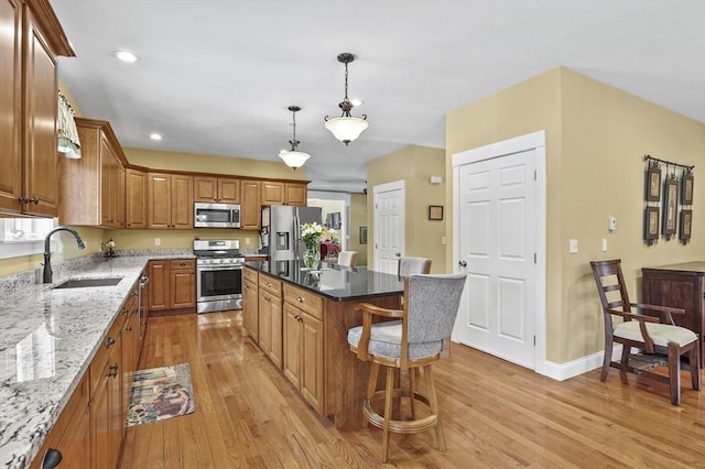 kitchen featuring appliances with stainless steel finishes, light wood-style floors, brown cabinetry, a sink, and a kitchen island