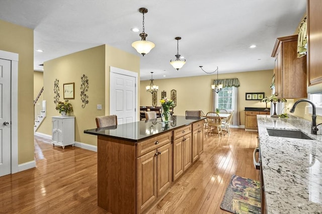 kitchen with dark stone countertops, a sink, light wood-style flooring, and an inviting chandelier