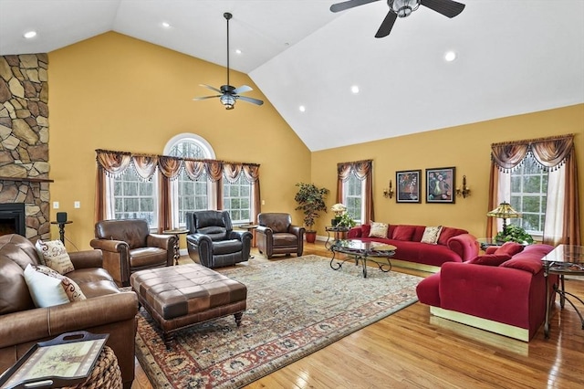 living room with plenty of natural light, high vaulted ceiling, wood finished floors, and a stone fireplace