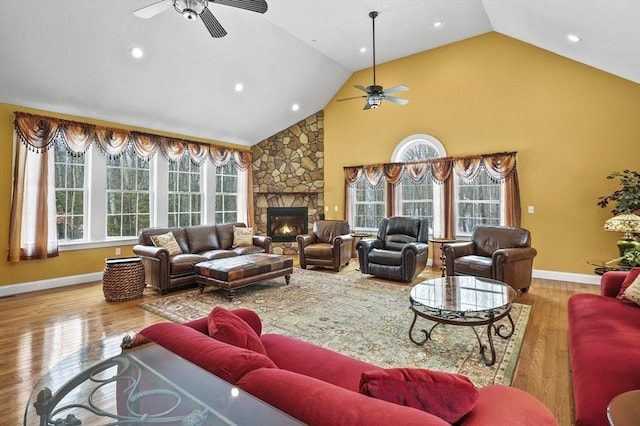 living room with high vaulted ceiling, a ceiling fan, a stone fireplace, and wood finished floors