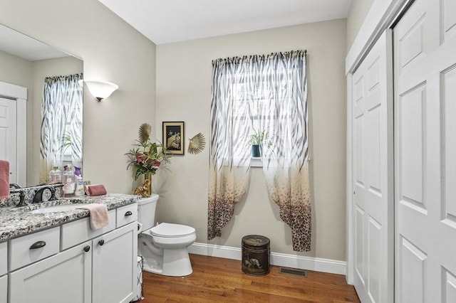 half bathroom featuring toilet, wood finished floors, visible vents, vanity, and baseboards