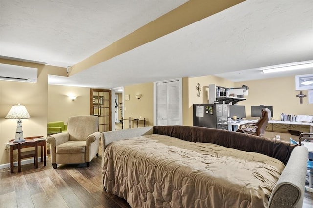 bedroom featuring a textured ceiling, a wall unit AC, hardwood / wood-style flooring, baseboards, and a closet