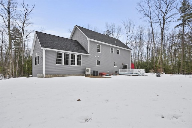 snow covered house featuring roof with shingles, cooling unit, and a wooden deck