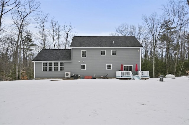 snow covered rear of property with a shingled roof, central AC unit, and a deck