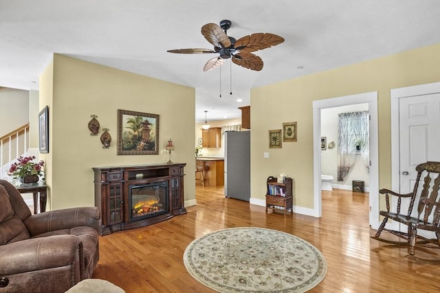 living room featuring light wood-style flooring, baseboards, ceiling fan, and a glass covered fireplace