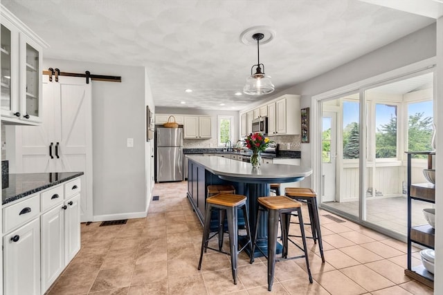 67 Hillside St, Rowley, MA 01969 - kitchen featuring stainless steel appliances, a kitchen breakfast bar, a barn door, white cabinetry, and tasteful backsplash