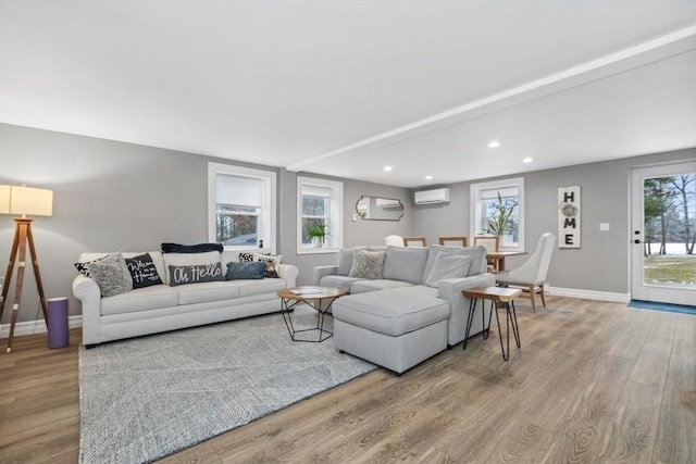 living room featuring a healthy amount of sunlight, a wall mounted AC, and light wood-type flooring