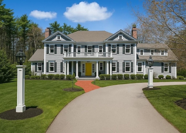 view of front of home featuring covered porch, a chimney, a balcony, and a front yard