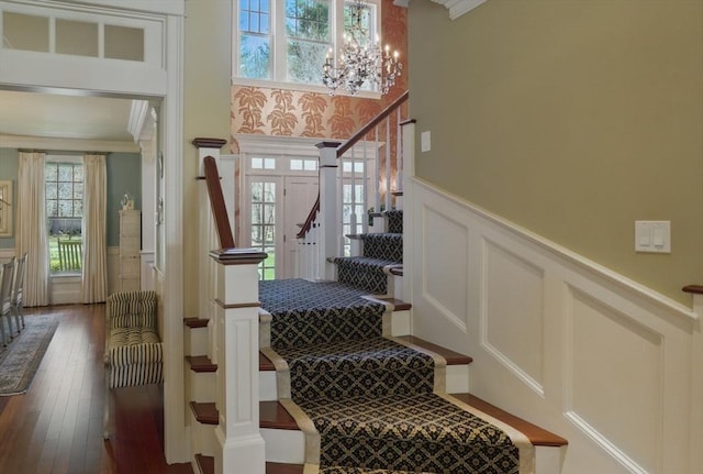 stairs featuring crown molding, a decorative wall, a chandelier, a wainscoted wall, and hardwood / wood-style flooring