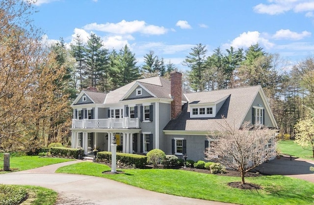 view of front of property featuring covered porch, a chimney, a front yard, and a balcony