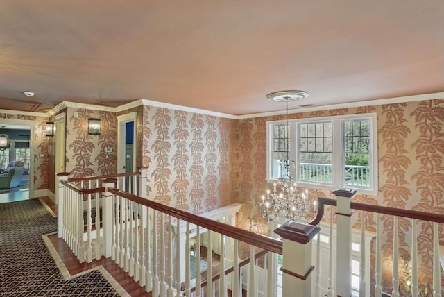 corridor featuring a notable chandelier, wallpapered walls, an upstairs landing, and ornamental molding
