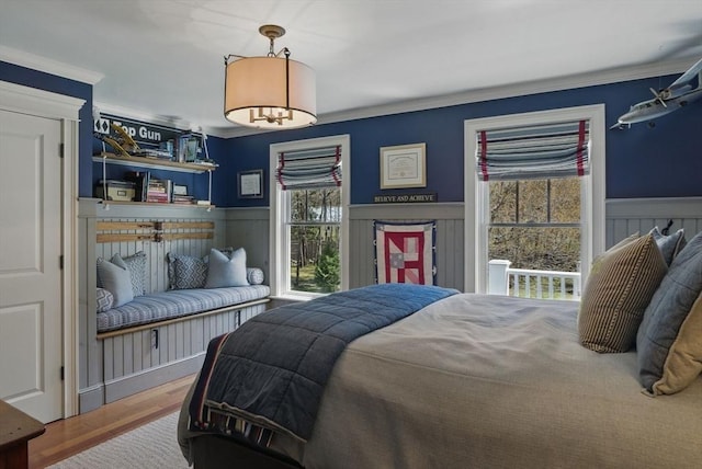 bedroom featuring multiple windows, ornamental molding, wainscoting, and wood finished floors