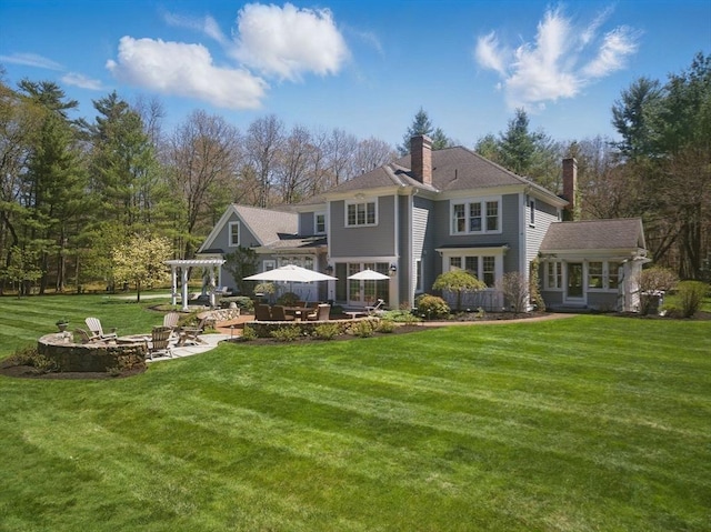 back of house featuring a pergola, a chimney, a patio area, a lawn, and an outdoor fire pit