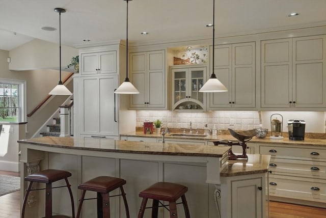 kitchen featuring stone countertops, decorative backsplash, a kitchen island with sink, and a breakfast bar