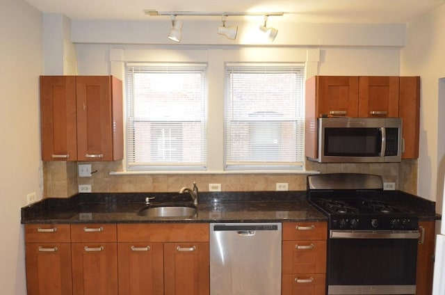 kitchen with tasteful backsplash, appliances with stainless steel finishes, dark stone counters, and a sink