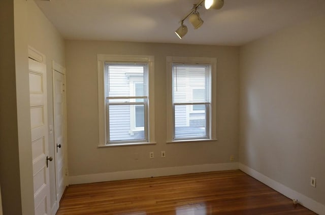 empty room with wood finished floors, rail lighting, and baseboards