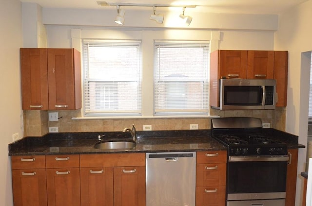 kitchen with stainless steel appliances, dark stone countertops, a sink, and a healthy amount of sunlight