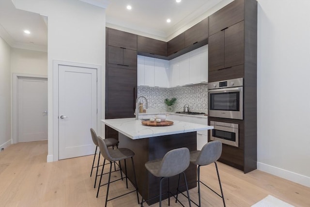 kitchen with stainless steel appliances, a kitchen breakfast bar, a kitchen island with sink, and light hardwood / wood-style flooring