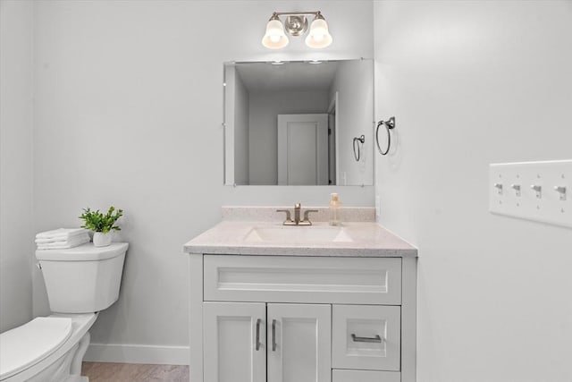 half bathroom with toilet, vanity, baseboards, and wood finished floors