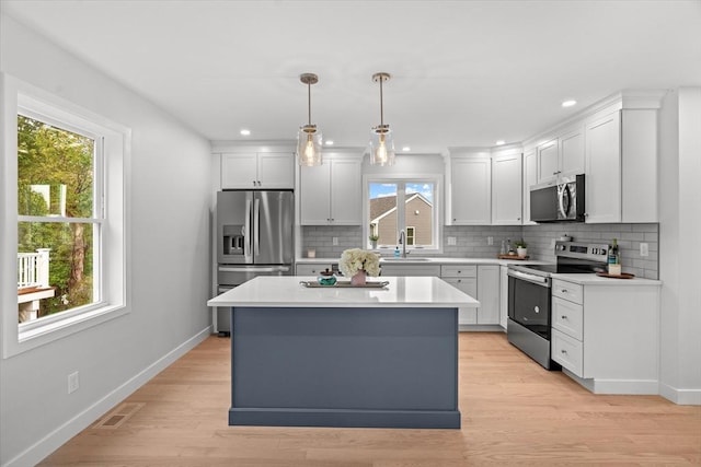 kitchen with appliances with stainless steel finishes, a kitchen island, baseboards, tasteful backsplash, and light countertops