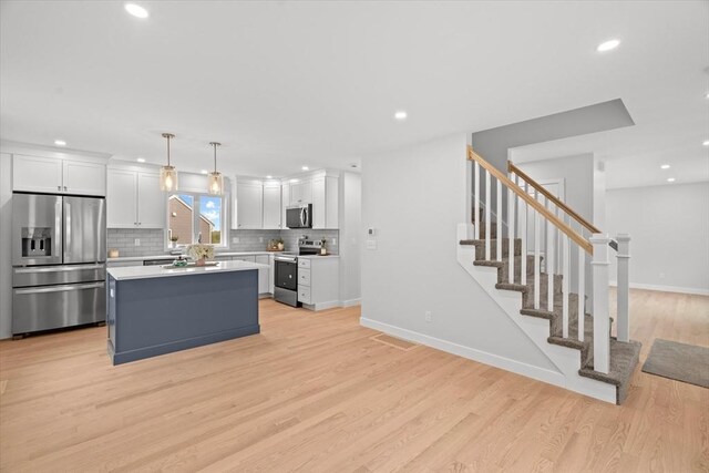 kitchen with stainless steel appliances, white cabinetry, light wood-style floors, recessed lighting, and a kitchen island