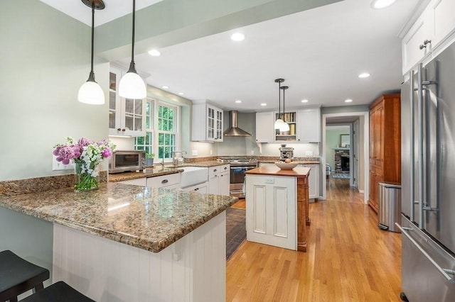 5 Whipple Rd, Hamilton, MA 01982 - kitchen with stainless steel appliances, wall chimney exhaust hood, light wood-type flooring, glass insert cabinets, and a peninsula