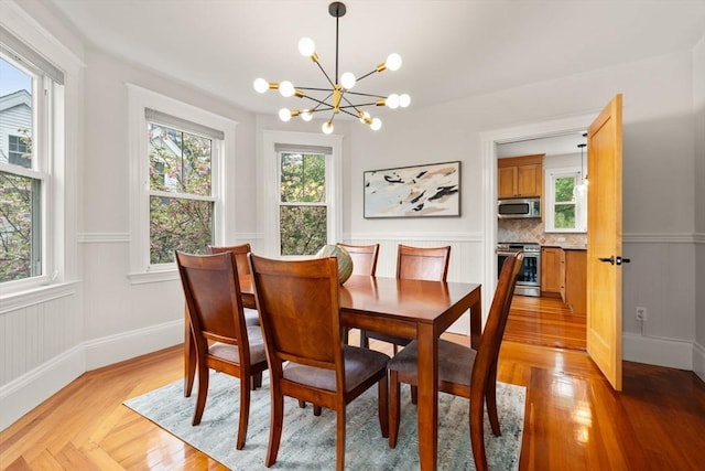 dining space featuring a chandelier, a wainscoted wall, light wood-type flooring, and baseboards