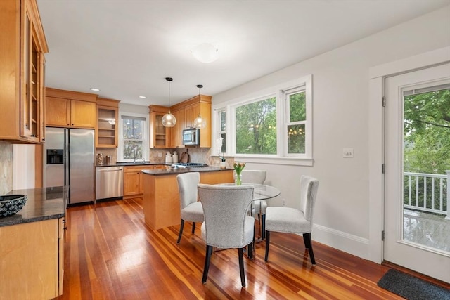 kitchen featuring appliances with stainless steel finishes, wood finished floors, glass insert cabinets, a peninsula, and decorative backsplash