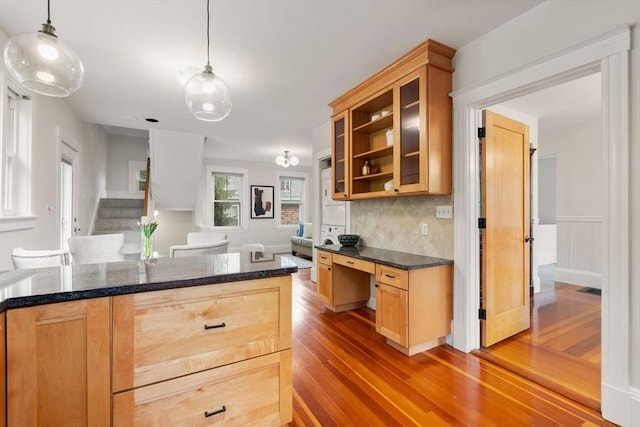 kitchen featuring light wood-type flooring, backsplash, glass insert cabinets, decorative light fixtures, and dark stone countertops