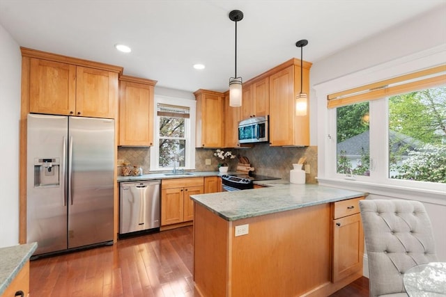 kitchen featuring appliances with stainless steel finishes, a sink, a peninsula, decorative backsplash, and dark wood-type flooring