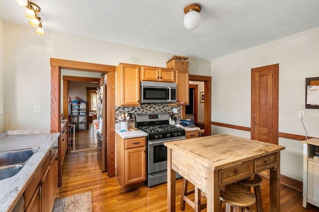 kitchen with light wood-type flooring, appliances with stainless steel finishes, decorative backsplash, and sink