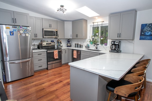 kitchen with vaulted ceiling with skylight, sink, kitchen peninsula, gray cabinetry, and appliances with stainless steel finishes