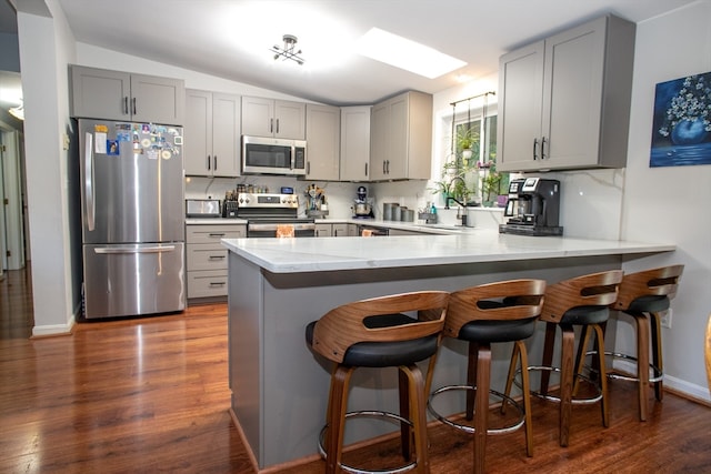 kitchen featuring stainless steel appliances, kitchen peninsula, dark wood-type flooring, and gray cabinetry