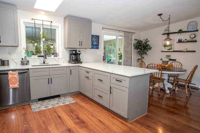 kitchen with a skylight, light wood-type flooring, sink, dishwasher, and kitchen peninsula